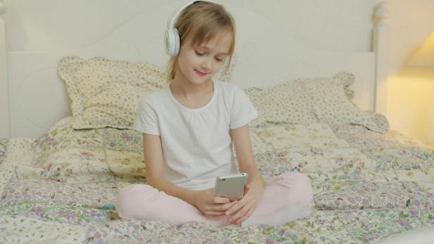 Ein Mädchen sitzt mit ihrem Smartphone am Bett 