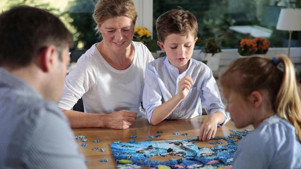Eine Familie sitzt gemeinsam am Tisch und setzt ein großes Ravensburger-Puzzle mit buntem Meeresmotiv zusammen.