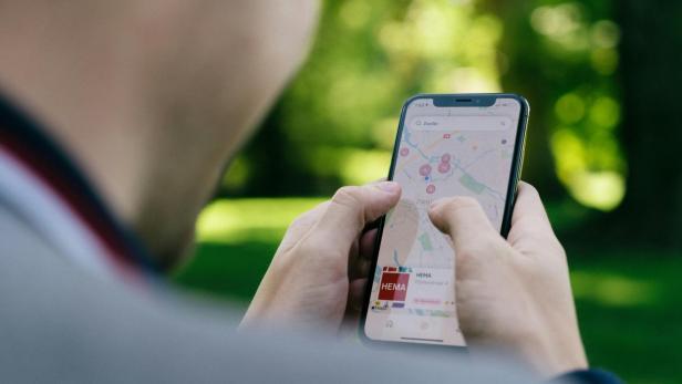 Person hält Handy in der Hand, auf dem Google Maps geöffnet ist, Hintergrund ist ein Park