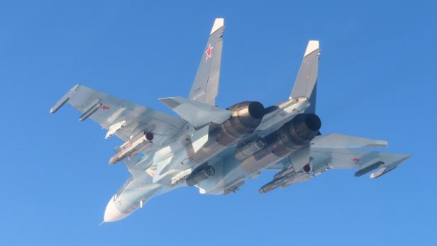 Russischer Kampfjet Su-30SM mit Raketenbewaffnung im Flug vor blauem Himmel.
