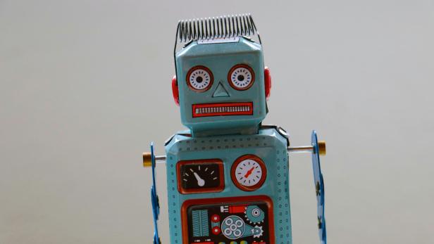 Blechspielzeug-Roboter mit aufgemalten Anzeigen und Spiralfeder auf dem Kopf vor grauem Hintergrund.