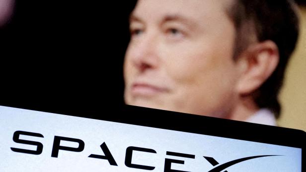 Elon Musk blickt über das SpaceX-Logo auf einem Bildschirm.