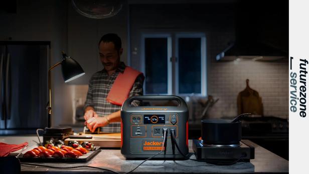 Ein Mann kocht in einer dunklen Küche mit einer tragbaren Powerstation und Lampe auf der Arbeitsplatte.