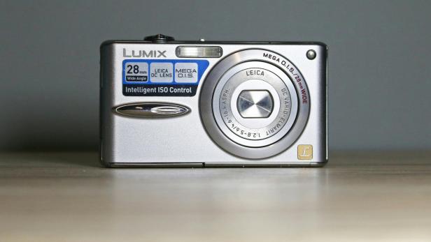 Silberne Kompaktkamera der Marke Lumix mit Leica-Objektiv auf hellem Untergrund.