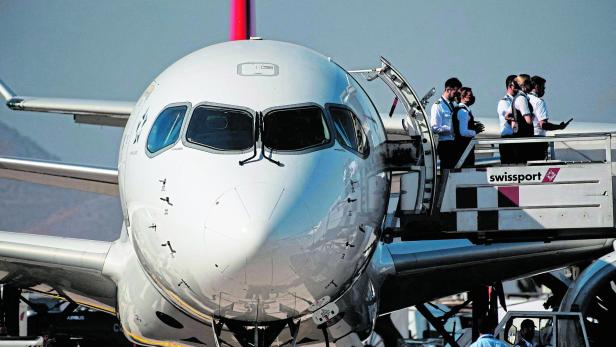 Ein Flugzeug steht am Boden, während mehrere Crewmitglieder an einer geöffneten Tür auf einer Fluggastbrücke stehen.