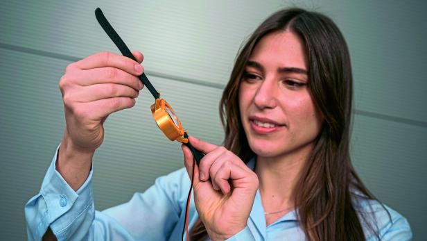 Eine Frau hält eine orangefarbene Armbanduhr mit schwarzem Armband und betrachtet sie aufmerksam.