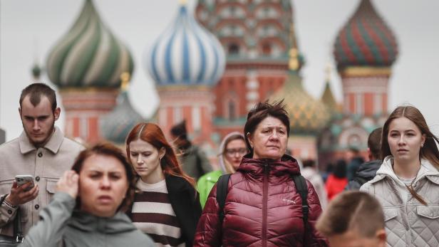 Mehrere Menschen gehen vor den bunten Zwiebeltürmen der Basilius-Kathedrale in Moskau entlang.