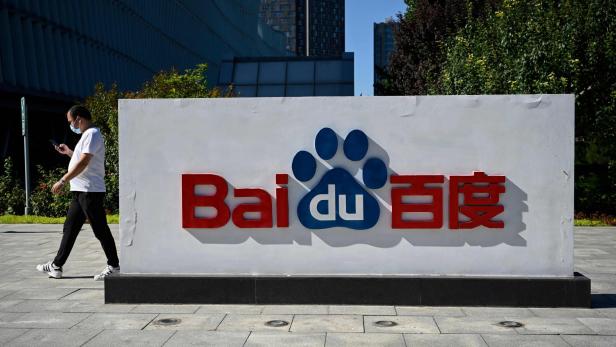Ein Mann mit Maske geht an einem großen Baidu-Logo mit Pfotenabdruck im Freien vorbei.