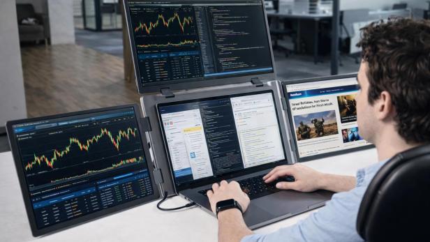 Mann arbeitet an einem Laptop mit drei zusätzlichen, angeschlossenen Bildschirmen.