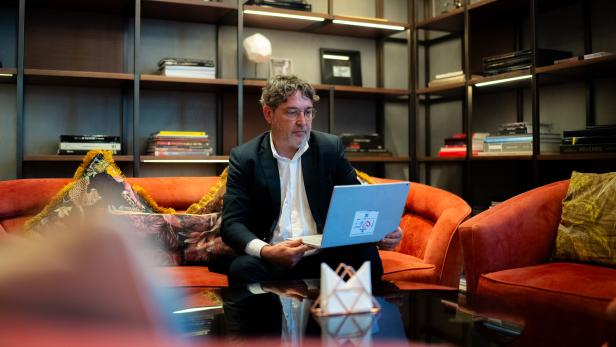 Mann im Anzug arbeitet mit Laptop auf orangefarbenem Sofa vor Bücherregal.