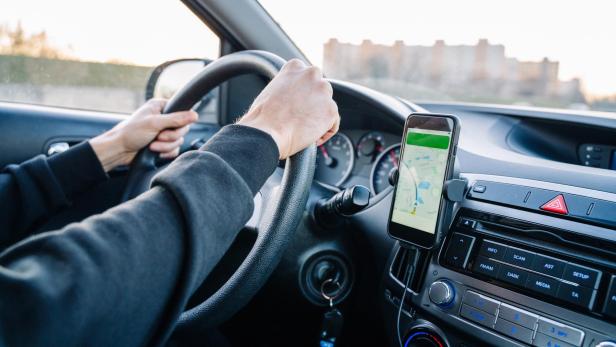 Eine Person fährt ein Auto und nutzt ein Smartphone mit Navigations-App an der Armatur.