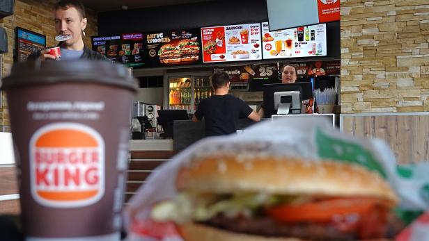 In einem Burger King Restaurant stehen ein Burger, ein Getränk und Kunden vor der Theke.