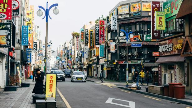 Belebte Straße in Südkorea mit zahlreichen Geschäften und bunten Schildern auf Koreanisch.