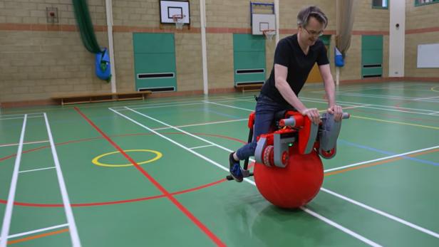 Ein Mann fährt mit einem Gymnastikball-E-Bike durch eine Turnhalle