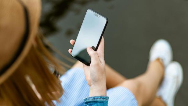 Person mit Hut auf dem Kopf hält ihr Smartphone vor sich.