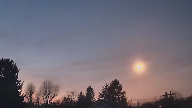 Leuchtender Meteor am Abendhimmel über einer Häuser- und Baumreihe.