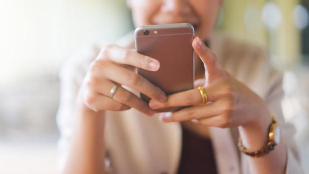 Eine Person hält ein Smartphone mit beiden Händen vor sich. (Symbolbild)