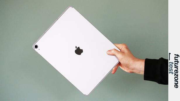 Eine Hand hält ein silbernes iPad Air 13 vor grünem Hintergrund.
