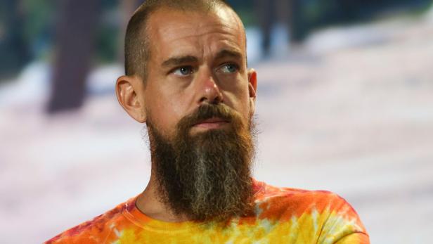 Ein Mann mit Vollbart und Glatze trägt ein buntes Batik-T-Shirt und blickt nachdenklich zur Seite.