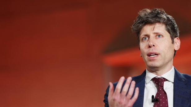 Sam Altman mit Anzug und Krawatte gestikuliert vor einem orangefarbenen Hintergrund.