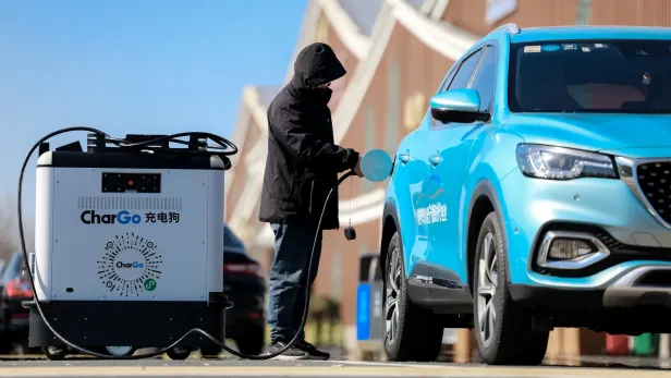 Eine Person lädt ein blaues Elektroauto mit einem mobilen Lade-Roboter namens CharGo auf.