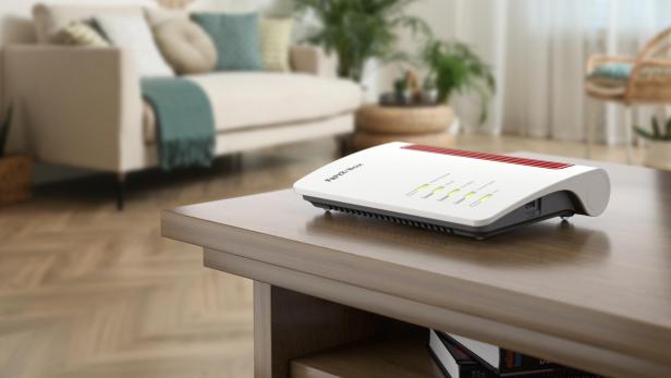 Ein WLAN-Router mit leuchtenden Anzeigen steht auf einem Holztisch in einem gemütlich eingerichteten Wohnzimmer.