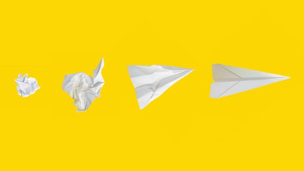 zusammengeknülltes Papier und Papierflieger vor gelbem Hintergrund