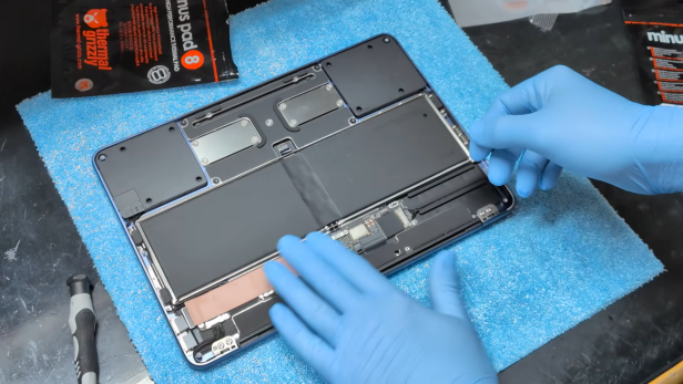 Geöffnetes MacBook Neo mit sichtbarem Innenleben und blauen Handschuhen bei der Montage.