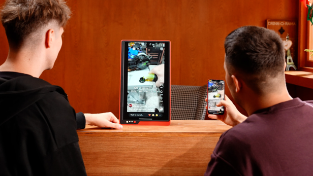 Zwei Personen betrachten ein Smartphone-Display, das auf einen größeren tragbaren Monitor gespiegelt wird.