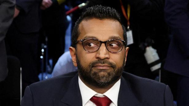 Ein Mann mit Brille und roter Krawatte sitzt im Anzug an einem Tisch und blickt zur Seite.