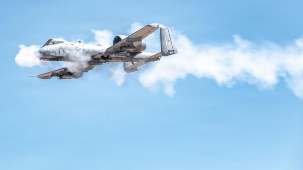 Kampfflugzeug fliegt am Himmel und schießt mit der Bordkanone