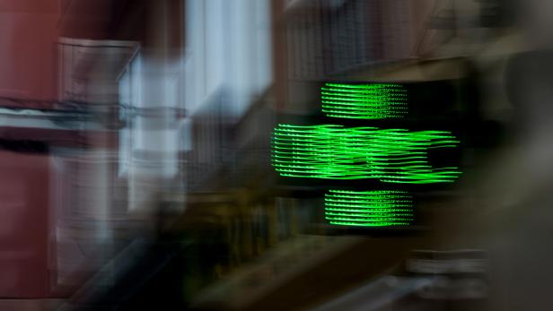 Verschwommenes grünes LED-Kreuz leuchtet vor unscharfem Hintergrund in einer Stadt.