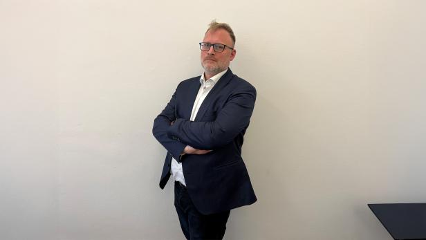 Ein Mann lehnt in einem Anzug an einer Wand 