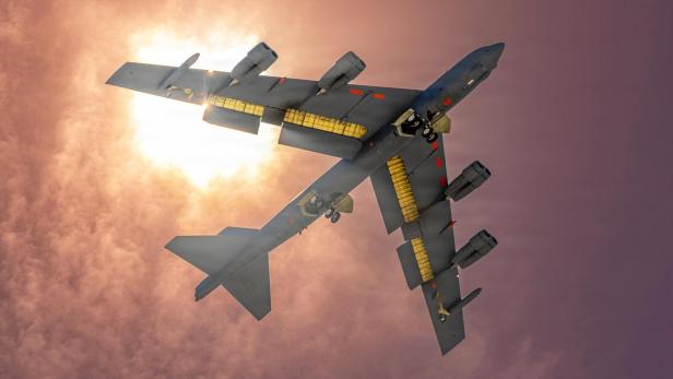 Ein B-52-Bomber fliegt mit ausgefahrenem Fahrwerk vor der Sonne durch bewölkten Himmel.