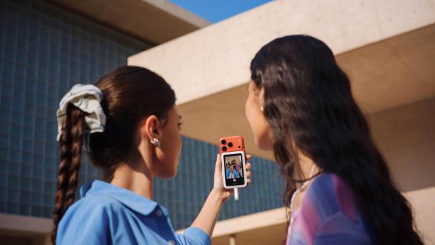 Zwei Frauen machen ein Selfie mit einem Smartphone und magnetischem Zweitbildschirm im Freien.