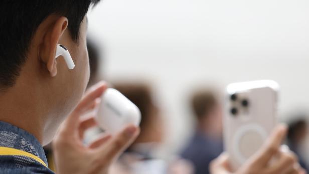 Eine Person hält AirPods-Kopfhörer und ein iPhone in der Hand