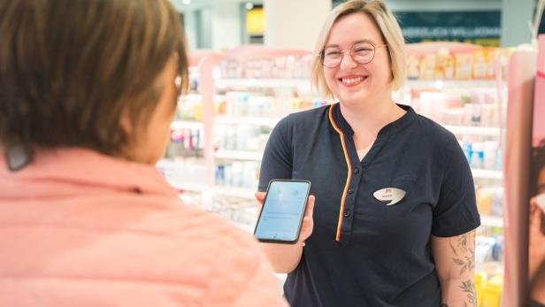 dm-Mitarbeiterin mit Smartphone in der Hand in Filiale mit Kundin