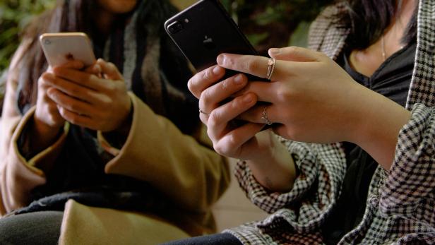 Zwei Personen halten nebeneinander sitzend jeweils ein iPhone in den Händen.