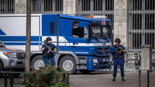 Zwei bewaffnete Polizisten in Schutzkleidung stehen vor einem blauen Lastwagen vor einem historischen Gebäude.