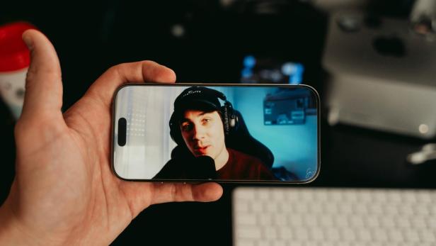 Hand hält Smartphone mit Video eines jungen Mannes mit Kopfhörern und Mikrofon.