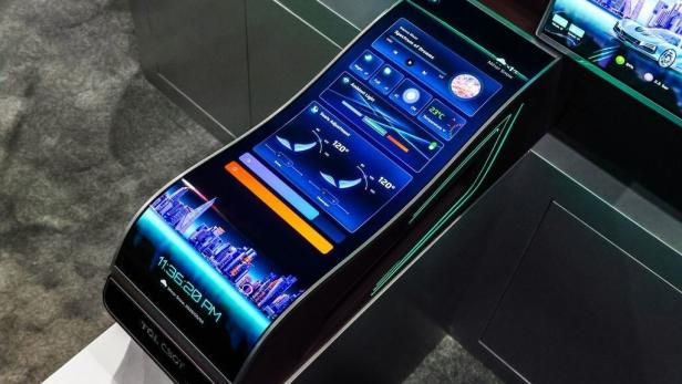 Großer, gebogener Touchscreen in einer Autoarmlehne mit farbigen Anzeigen und Bedienelementen.