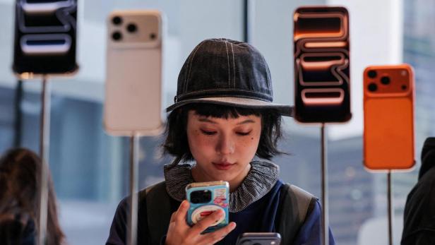 Eine Frau mit Hut betrachtet zwei Smartphones vor ausgestellten Handyhüllen.