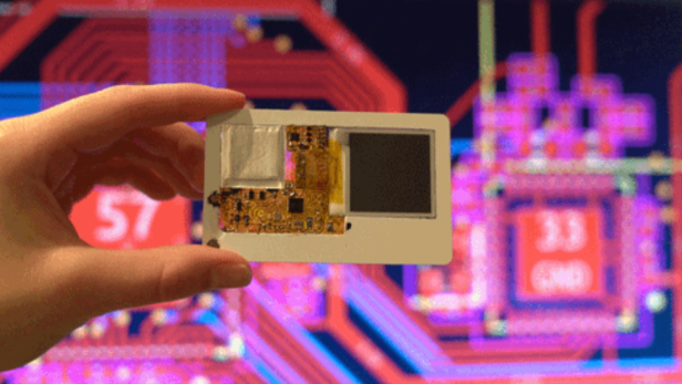 Eine Hand hält einen dünnen Mini-Computer im Kreditkartenformat vor einem bunten Schaltplan.