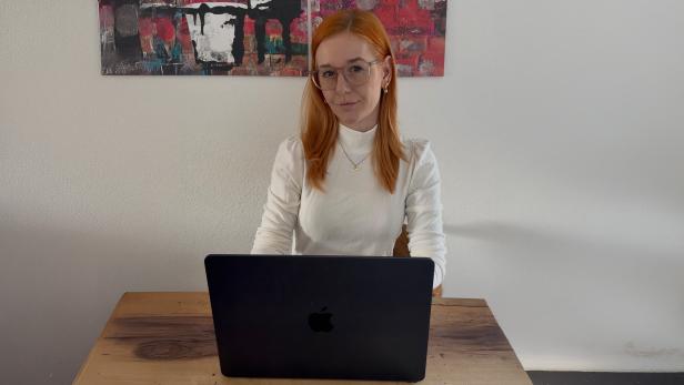 Eine rothaarige Frau in einem weißen Langshirt vor einem schwarzen Laptop 