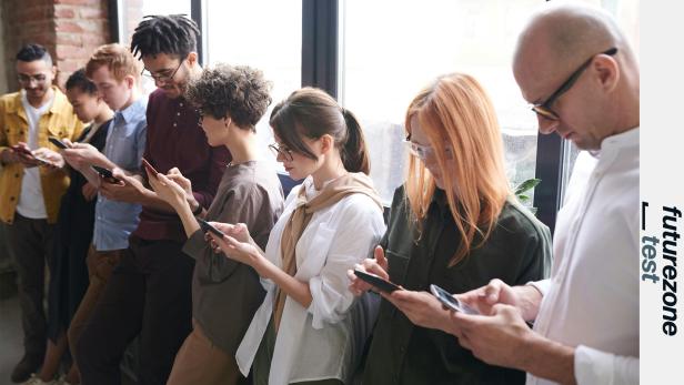 Mehrere Menschen stehen nebeneinander und tippen konzentriert auf ihre Smartphones.