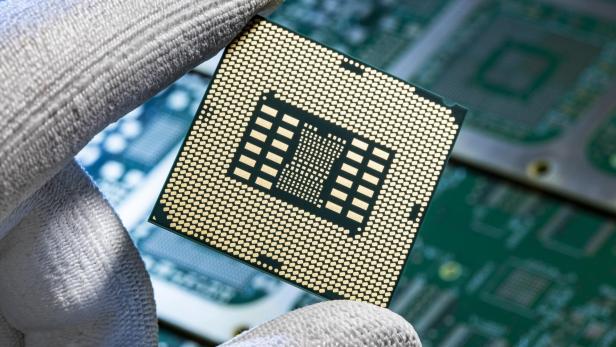 Hand mit Handschuh hält einen Mikrochip über einer Leiterplatte.