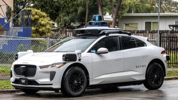 Weißes autonomes Elektroauto mit Sensoren und Kameras auf dem Dach und an den Seiten, mit der Aufschrift „Waymo“.