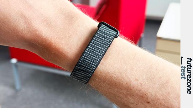 Graues Fitbit Air am Arm mit rotem Sessel im Hintergrund