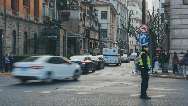 ein Polizist in gelber Warnweste auf einer Kreuzung, hinter ihm verschwommene abbiegende Autos