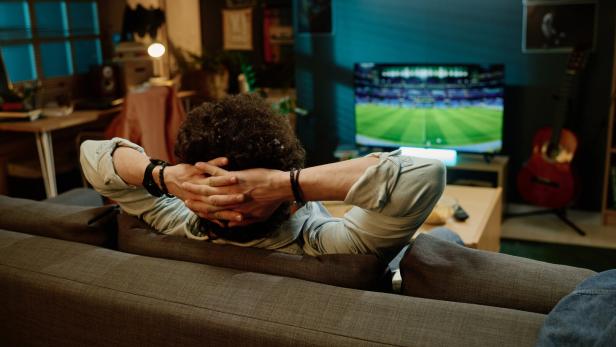 Ein Mann sitzt auf dem Sofa vor dem Fernseher.